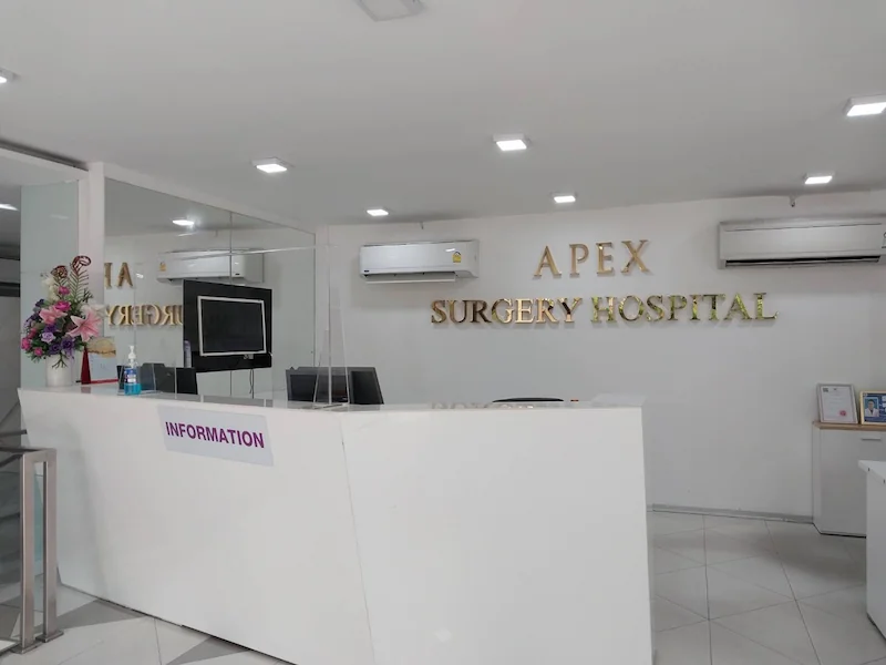 The Apex Surgery Hospital reception: a white information counter under gold APEX SURGERY HOSPITAL lettering, with a flower arrangement to one side.